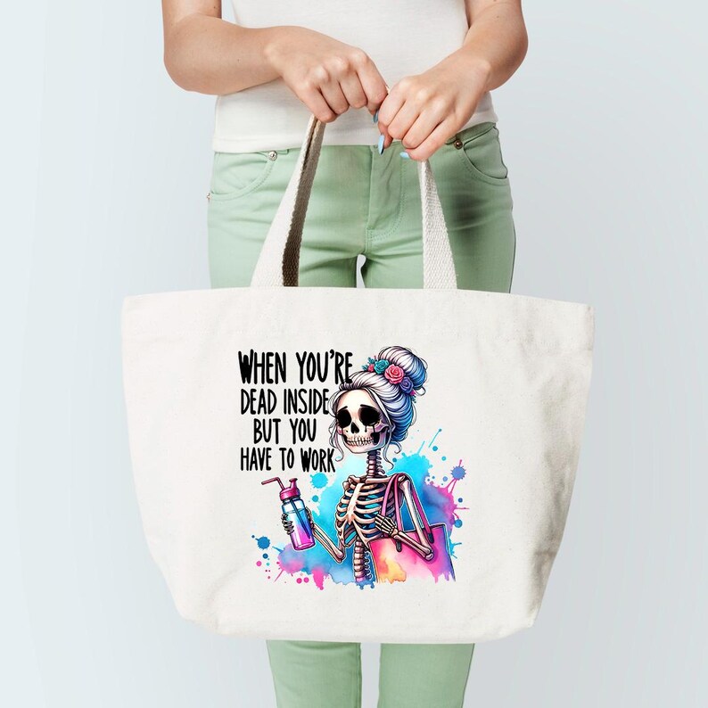 May include: White tote bag with a colorful graphic of a skeleton with a bun and flowers in her hair. The skeleton is holding a water bottle and a purse. The text on the bag reads "When you're dead inside but you have to work."