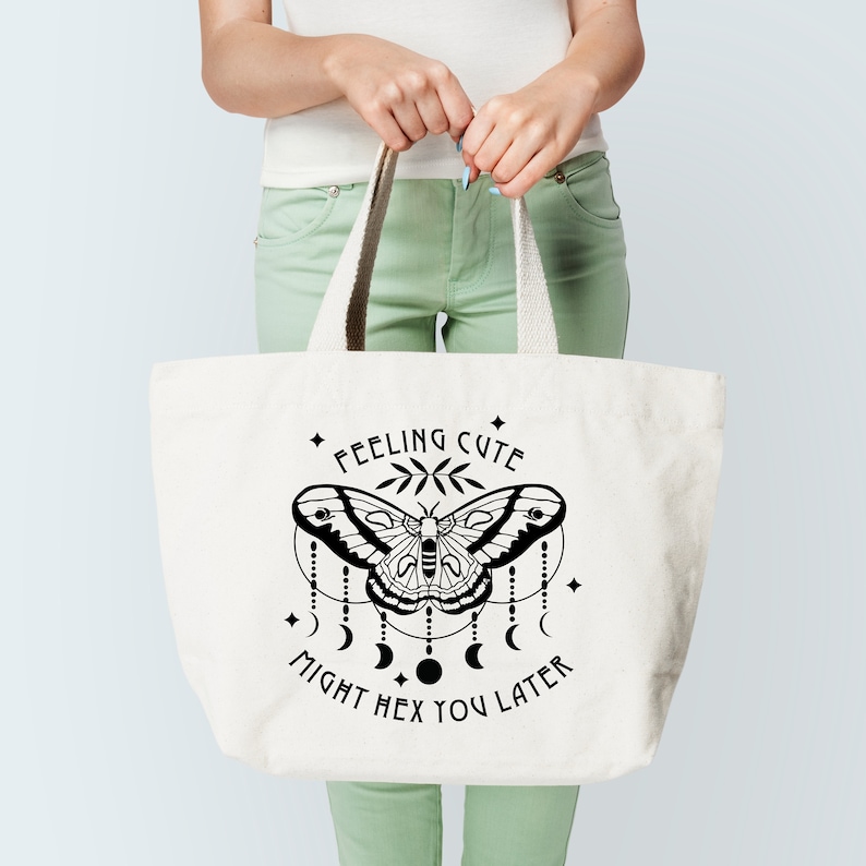 May include: A white tote bag with black text and a graphic of a moth with a crescent moon design. The text reads "Feeling Cute Might Hex You Later".