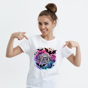 May include: White t-shirt with a colorful graphic print of bats and stars. The graphic says "Little Heathen" in black lettering.