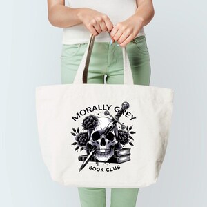 May include: A white tote bag with a black and white illustration of a skull with a sword through it. The text "Morally Grey Book Club" is printed below the skull.