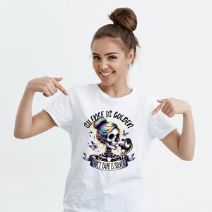 Puede incluir: Camiseta blanca con un gr&aacute;fico de una mujer esqueleto con cabello colorido sosteniendo un rollo de cinta adhesiva. El texto "Silence is Golden Duct Tape is Silver" est&aacute; impreso en la camiseta.