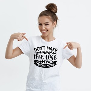 Puede incluir: Camiseta blanca con texto negro que dice "No me hagas usar mi voz de maestro" con un peque&ntilde;o gr&aacute;fico de manzana y un dise&ntilde;o de vid.