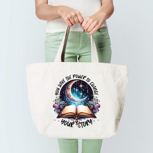 May include: A white tote bag with a design featuring a crescent moon, stars, and an open book. The text "YOU HAVE THE POWER TO CHANGE YOUR STORY" is printed on the bag. The bag has beige handles.