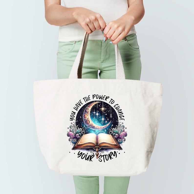 May include: A white tote bag with a design featuring a crescent moon, stars, and an open book. The text "YOU HAVE THE POWER TO CHANGE YOUR STORY" is printed on the bag. The bag has beige handles.