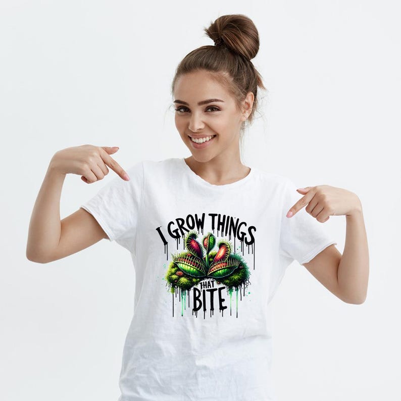 May include: White t-shirt featuring a colorful graphic of a Venus flytrap plant with the text "I GROW THINGS THAT BITE" in black. The design includes green, red, and yellow accents, with dripping paint effects.