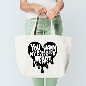 May include: A white tote bag with black handles and a black heart design that says "You warm my cold dark heart."