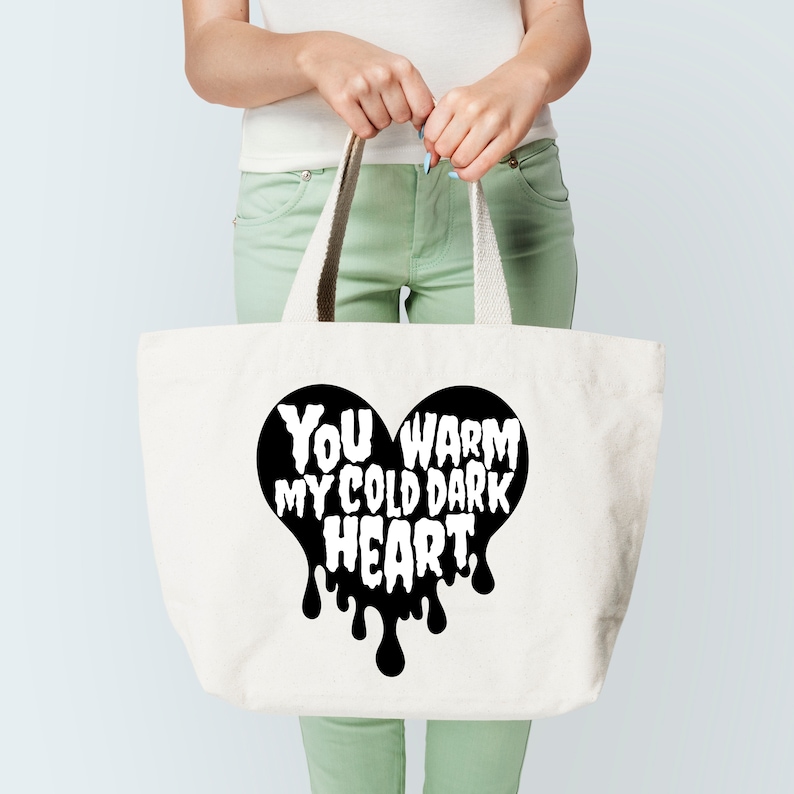 May include: A white tote bag with black handles and a black heart design that says "You warm my cold dark heart."