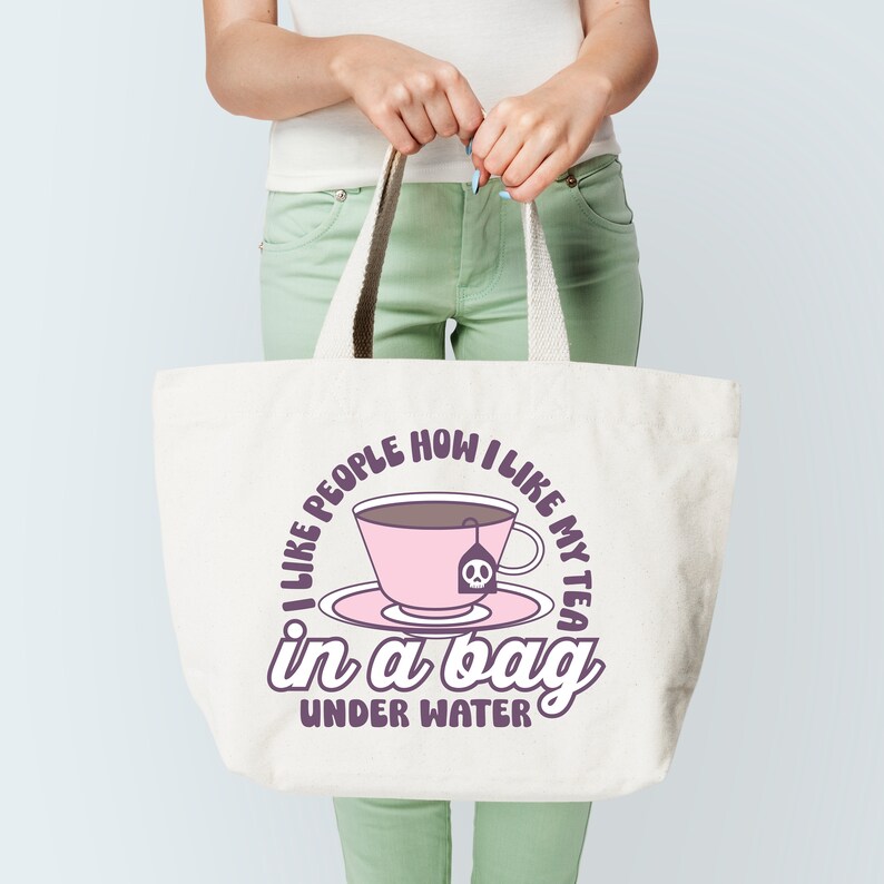 May include: A white tote bag with a purple design that says "I like people how I like my tea in a bag under water". The design also includes a pink teacup with a skull and crossbones tea bag.