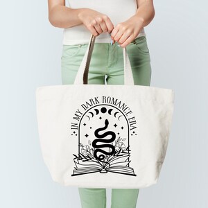 Puede incluir: Una bolsa de tela blanca con un dise&ntilde;o gr&aacute;fico negro que dice "In My Dark Romance Era" con una serpiente, un libro y lunas crecientes.