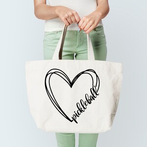 May include: A white canvas tote bag with black handles and a black heart design that says "pickleball" inside the heart.