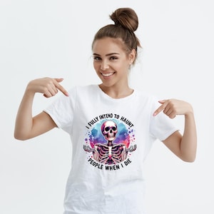 K&ouml;nnte beinhalten: Wei&szlig;es T-Shirt mit einem farbenfrohen Skelett-Grafik und dem Text "I FULLY INTEND TO HAUNT PEOPLE WHEN I DIE". Das Design zeigt einen rosa Sch&auml;del und einen Aquarell-Effekt, passend f&uuml;r Halloween.