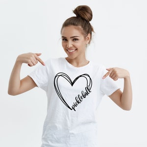 May include: White t-shirt with a black heart design and the word "pickleball" written inside the heart.