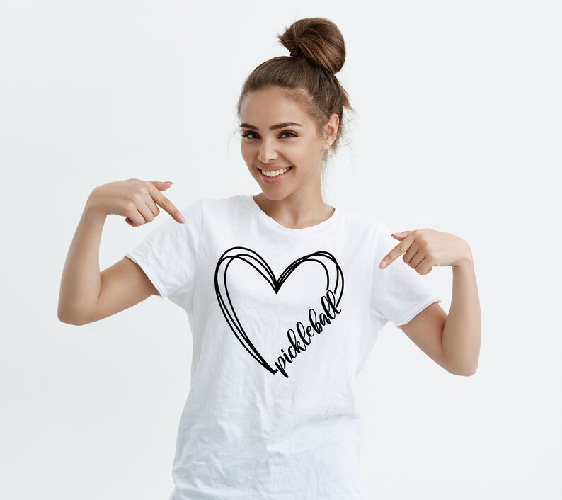 May include: White t-shirt with a black heart design and the word "pickleball" written inside the heart.