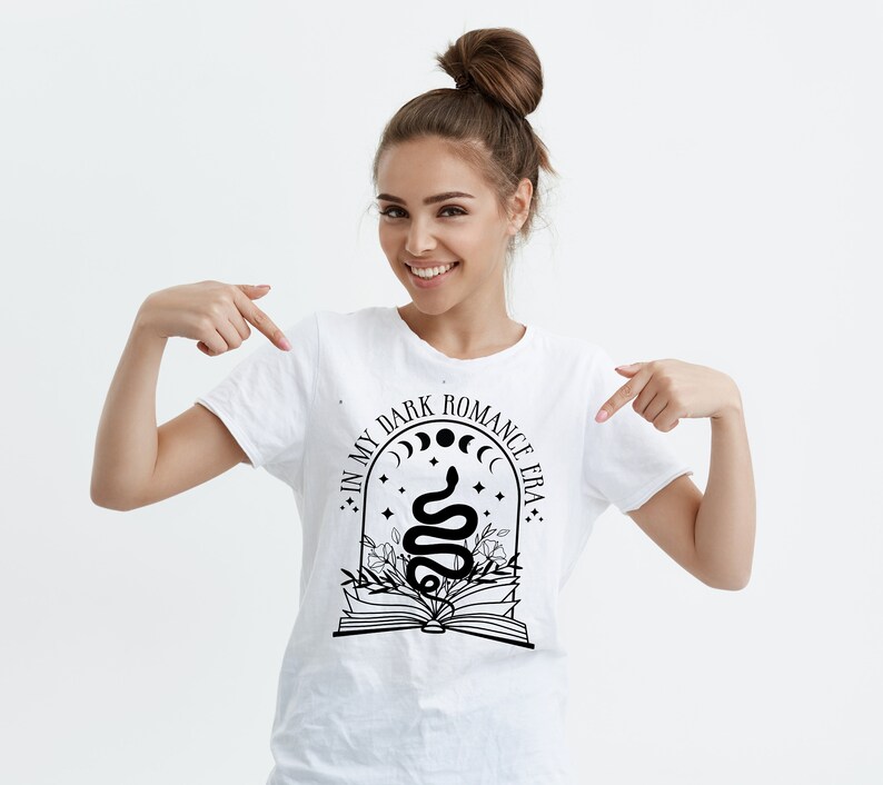 Puede incluir: Camiseta blanca con un dise&ntilde;o gr&aacute;fico negro que presenta una serpiente, un libro y el texto "In My Dark Romance Era."