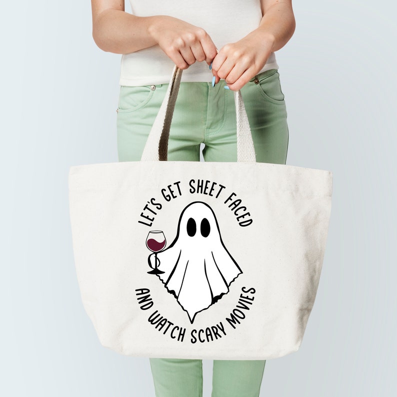 May include: White canvas tote bag featuring a black and white graphic of a ghost holding a glass of wine. The text on the bag reads "Let's get sheet faced and watch scary movies".