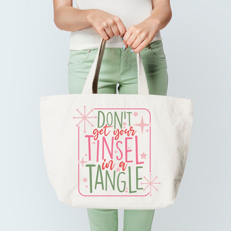 May include: A white canvas tote bag with the text "Don't get your tinsel in a tangle" in pink and green lettering with a starburst design.