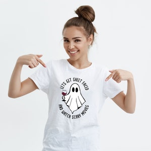 May include: White t-shirt with a black and white graphic of a ghost holding a glass of wine. The text on the shirt reads "Let's get sheet faced and watch scary movies".