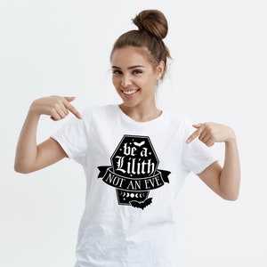 May include: A white t-shirt with a black graphic that says "be a Lilith not an Eve" with a crescent moon and stars design.