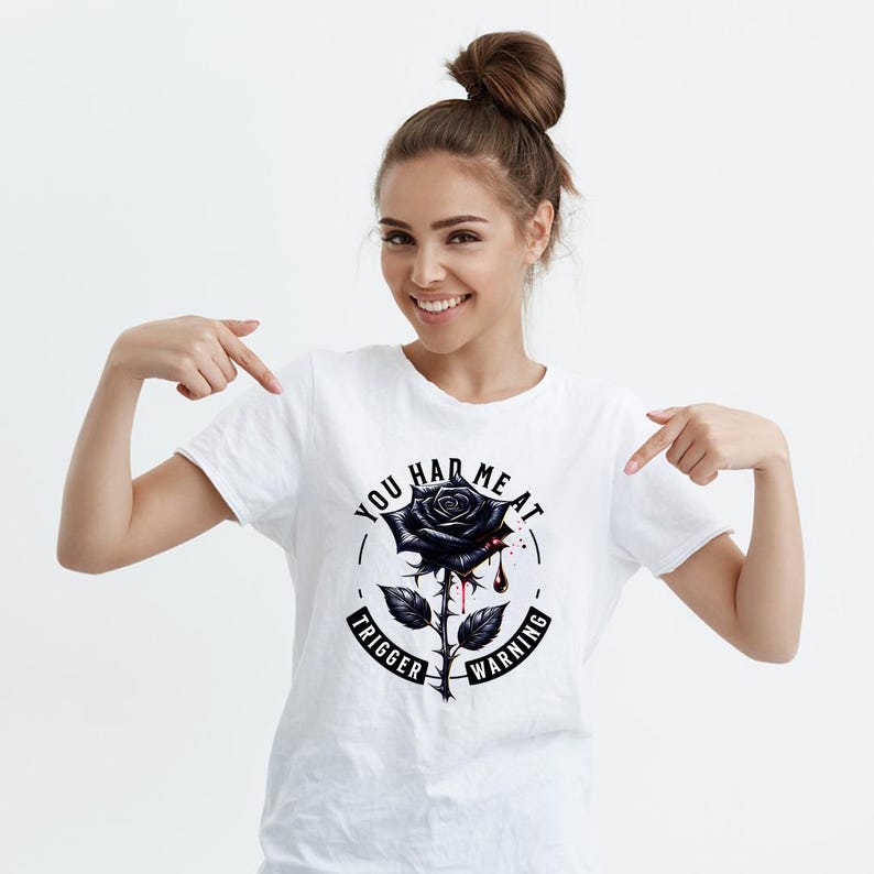 May include: White t-shirt with a black and white graphic of a black rose with a drop of blood. The text around the rose reads "You had me at trigger warning".