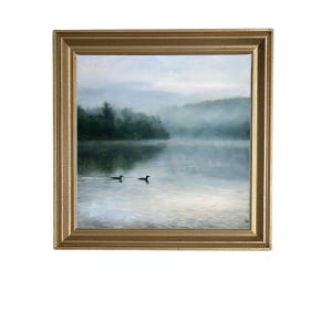 May include: A square landscape painting in a gold frame depicting two dark birds swimming on a calm, misty lake. The background features a dense, fog-covered forest line under a soft, pale sky, creating a serene and quiet atmosphere in the artwork.