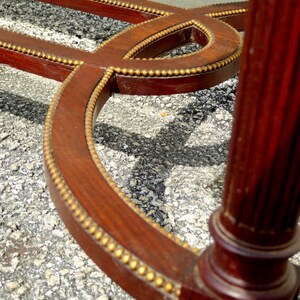 May include: A close-up of the base of a wooden table with a decorative gold trim. The table has a curved design and a square leg.