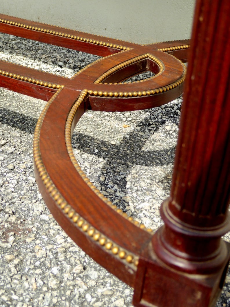 May include: A close-up of the base of a wooden table with a decorative gold trim. The table has a curved design and a square leg.