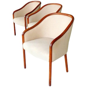 May include: Three white upholstered chairs with wooden frames. The chairs have a curved back and a rounded seat. The chairs are arranged in a row.