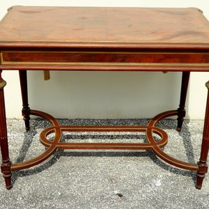 May include: A rectangular wooden table with a brown top and gold accents. The table has a lower shelf and four fluted legs.