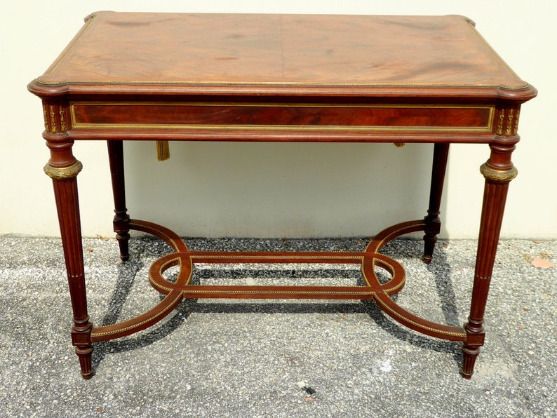May include: A rectangular wooden table with a brown top and gold accents. The table has a lower shelf and four fluted legs.