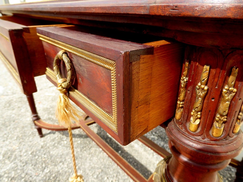May include: A mahogany console table with gold accents and two drawers. The table has a rope pull on the bottom drawer. The table is in the French Empire style.