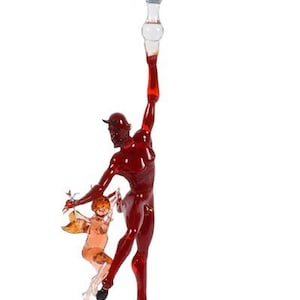 May include: A glass candlestick with a blue and white swirl design. A red glass figure of a devil holding a smaller glass figure of a cherub is attached to the candlestick.