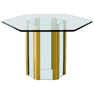 May include: A hexagonal glass table with a brass base. The table has a clear glass top and a gold-colored base.