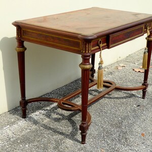 May include: A mahogany writing desk with a leather top, a single drawer, and gold accents. The desk has a curved, open base with a decorative design.