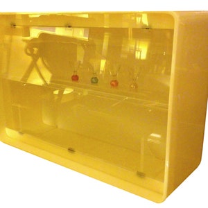 May include: A yellow acrylic display case with two shelves. The case has a rounded rectangular shape and is made of clear acrylic. The case is empty.