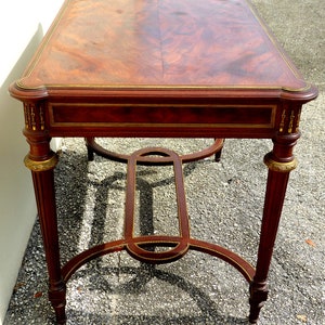 May include: A mahogany wood table with a rectangular top and a gold-painted trim. The table has a simple, elegant design with four legs and a lower shelf.