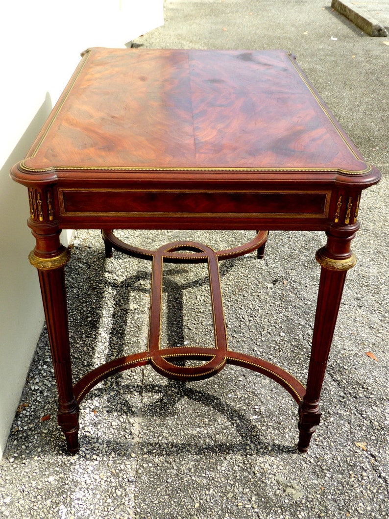 May include: A mahogany wood table with a rectangular top and a gold-painted trim. The table has a simple, elegant design with four legs and a lower shelf.