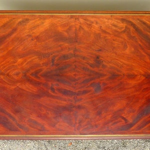 May include: A rectangular wooden table top with a rich mahogany finish. The table top has a decorative gold trim around the edge. The wood grain is visible and has a beautiful pattern.