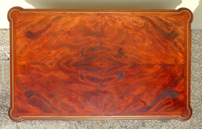 May include: A rectangular wooden table top with a rich mahogany finish. The table top has a decorative gold trim around the edge. The wood grain is visible and has a beautiful pattern.
