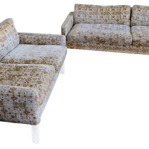 May include: A set of two sofas with a white and gold patterned fabric upholstery. The sofas have a modern design with a low profile and sleek lines. The legs are made of clear acrylic.