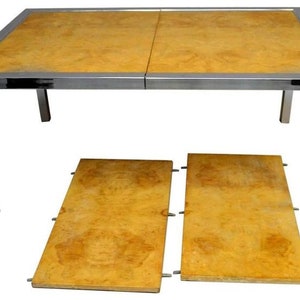 May include: A chrome-framed dining table with a wood top and two matching leaf extensions. The table is made of a light wood with a natural grain pattern.