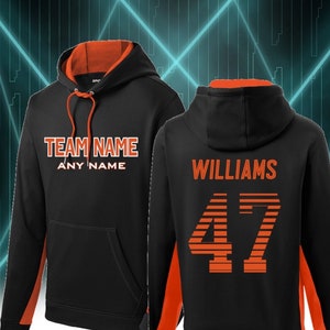 May include: Black hoodie with orange accents. The front of the hoodie has the text "TEAM NAME" and "ANY NAME". The back of the hoodie has the text "WILLIAMS" and the number "47" in a striped design.