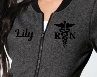 May include: A gray and black zip-up bomber jacket with a black medical symbol and the text "RN" and "Lily" on the front.