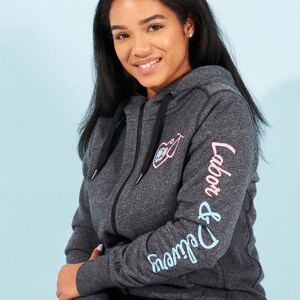 May include: A dark gray zip-up hoodie with a pink and blue graphic on the front and the text "Labor & Delivery" in blue and pink on the sleeve.