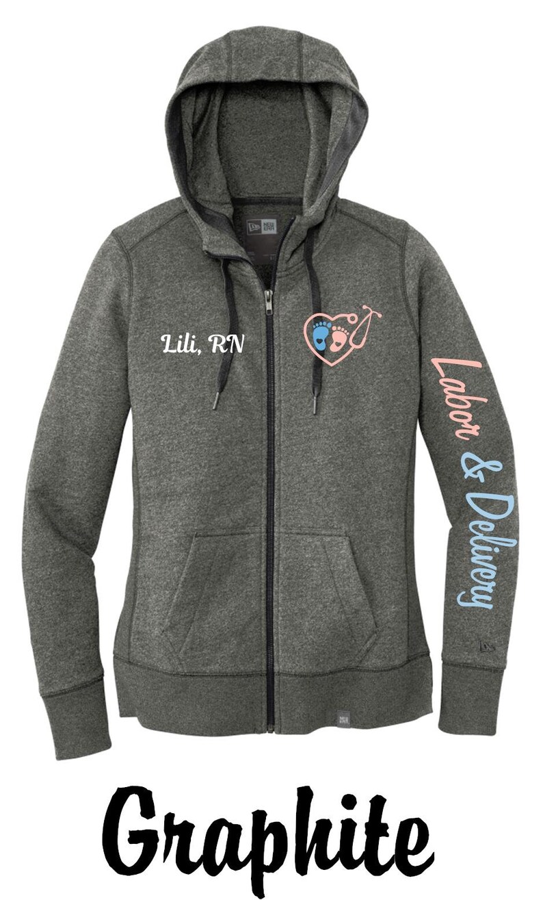 May include: A graphite grey zip-up hoodie with a black zipper and black drawstrings. The hoodie has a heart with baby footprints and a stethoscope on the front and the text "Lili, RN" below it. The left sleeve has the text "Labor & Delivery" in blue.