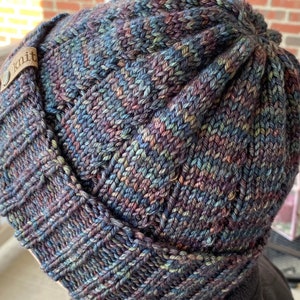 May include: A dark blue, green, and purple knitted beanie with a brown leather tag that says "knit".