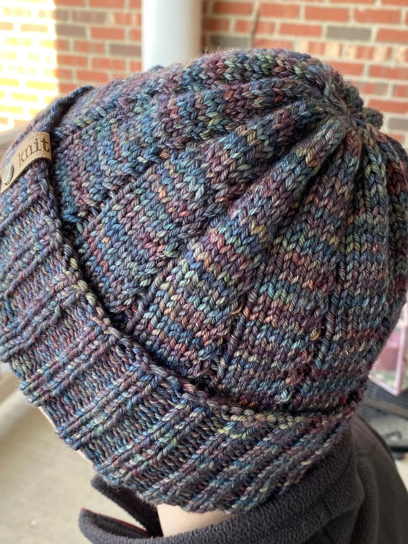May include: A dark blue, green, and purple knitted beanie with a brown leather tag that says "knit".