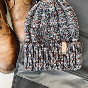 May include: A blue, brown, and gray knitted beanie with a brown leather tag that says "O knit".