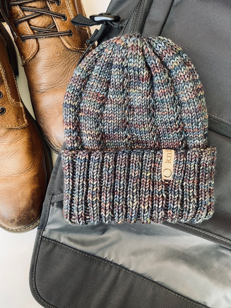 May include: A blue, brown, and gray knitted beanie with a brown leather tag that says "O knit".