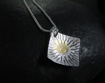 May include: A silver necklace with a square pendant featuring a sun design with a gold center.