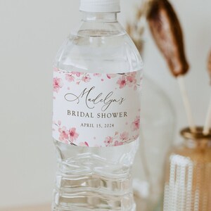 May include: A clear plastic water bottle with a white cap and a pink floral label that reads "Madelyn's Bridal Shower April 15, 2024".